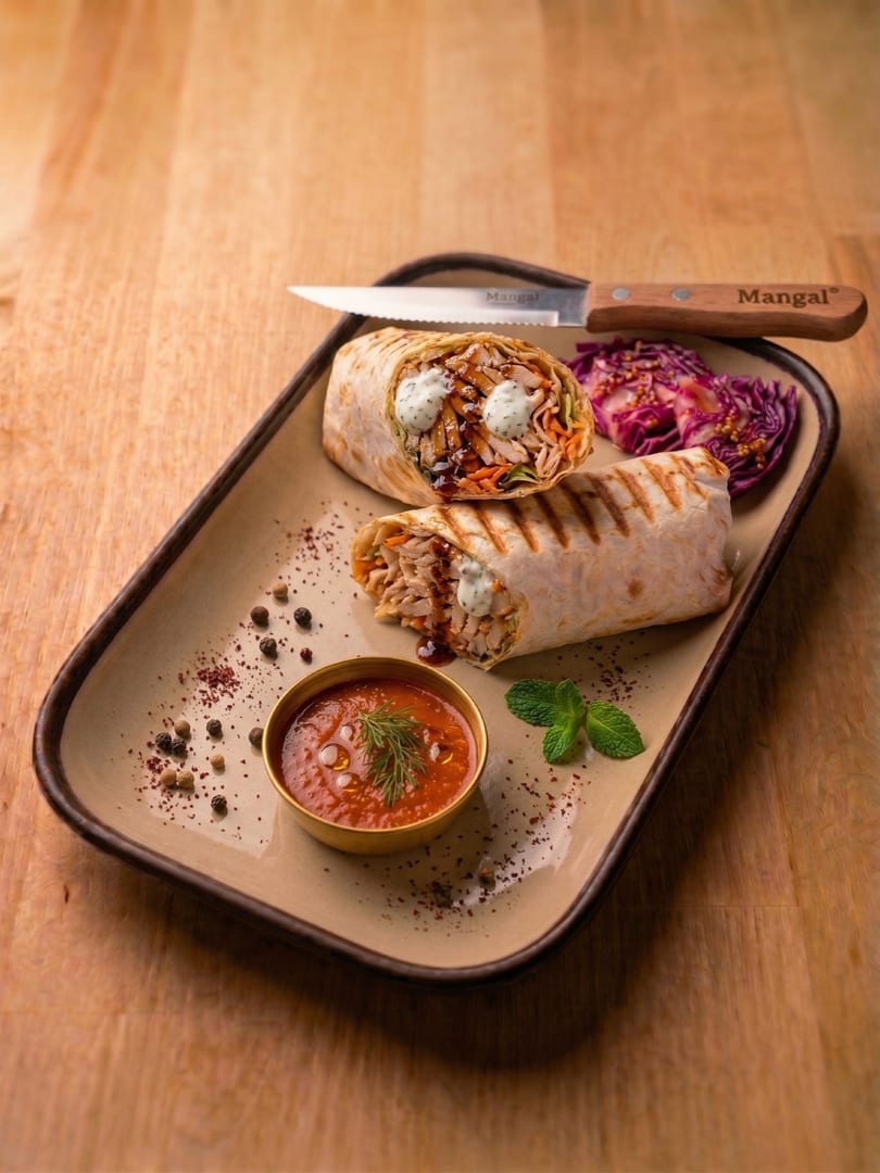 Two grilled chicken shawarma wraps with pickled cabbage, red sauce, and a branded Mangal knife on a tray.